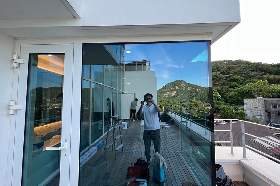 테라스 코너 통유리 앞에서 작업 중인 시공팀, 유리에 산과 하늘이 비치는 모습