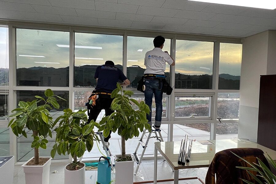 시공팀 두 명이 사다리 위에서 통유리에 필름을 붙이는 모습