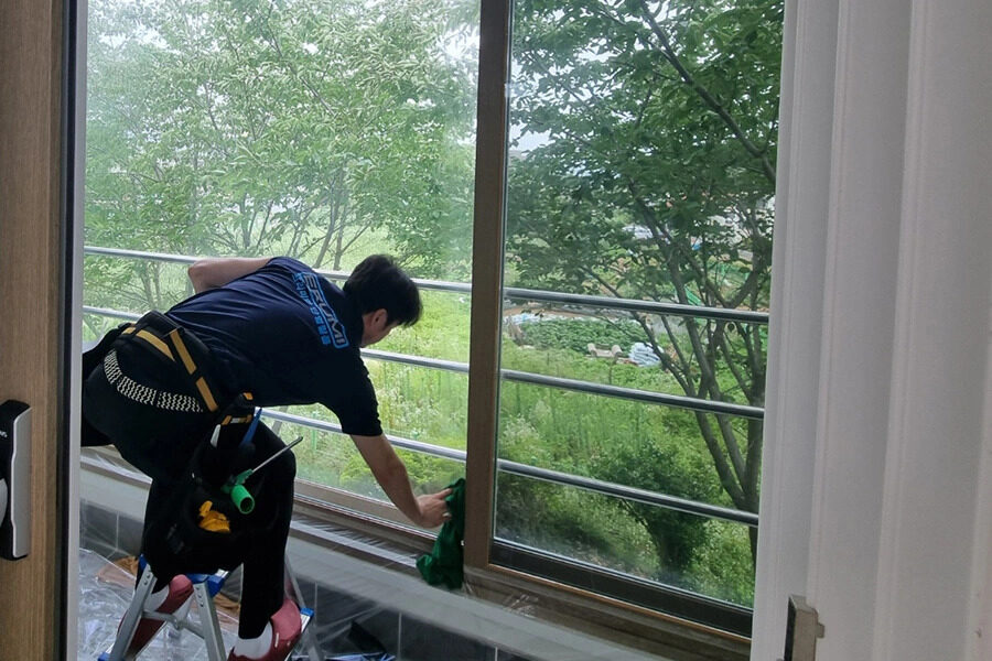 사다리 위에서 안전벨트를 착용하고 창틀 구석을 마감하는 시공팀