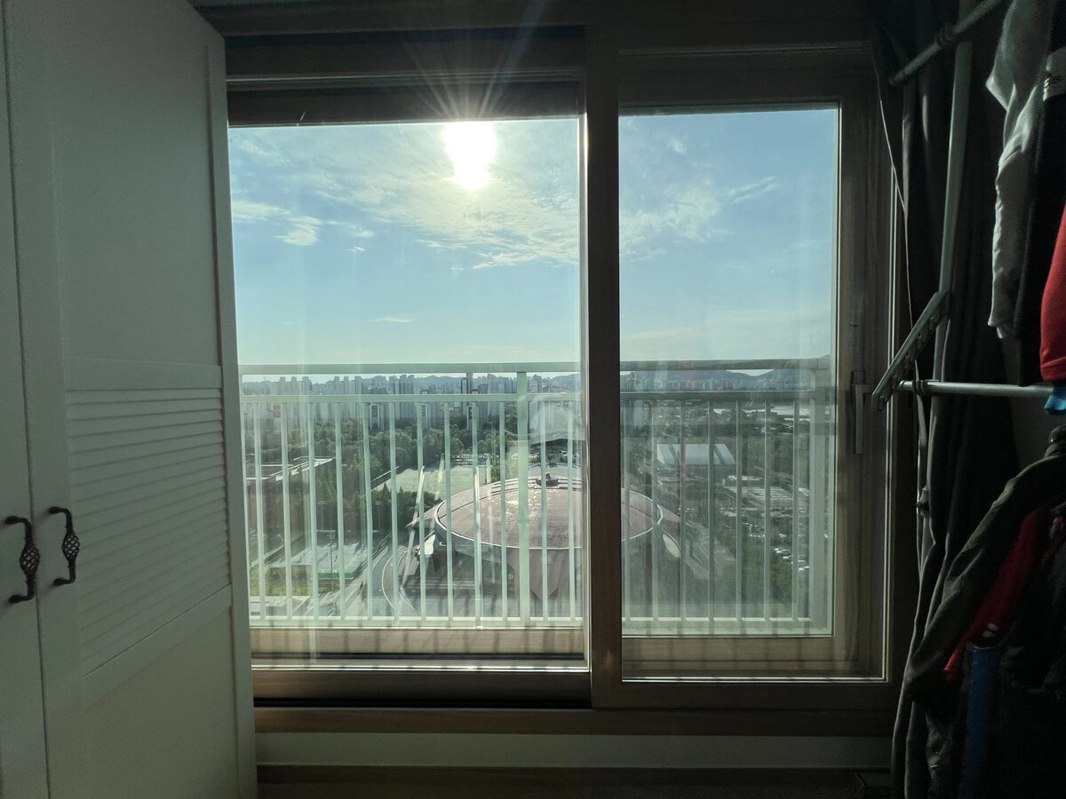 고층 세대 다른 방 창문에서 바라본 전경, 강한 햇빛과 도심 풍경