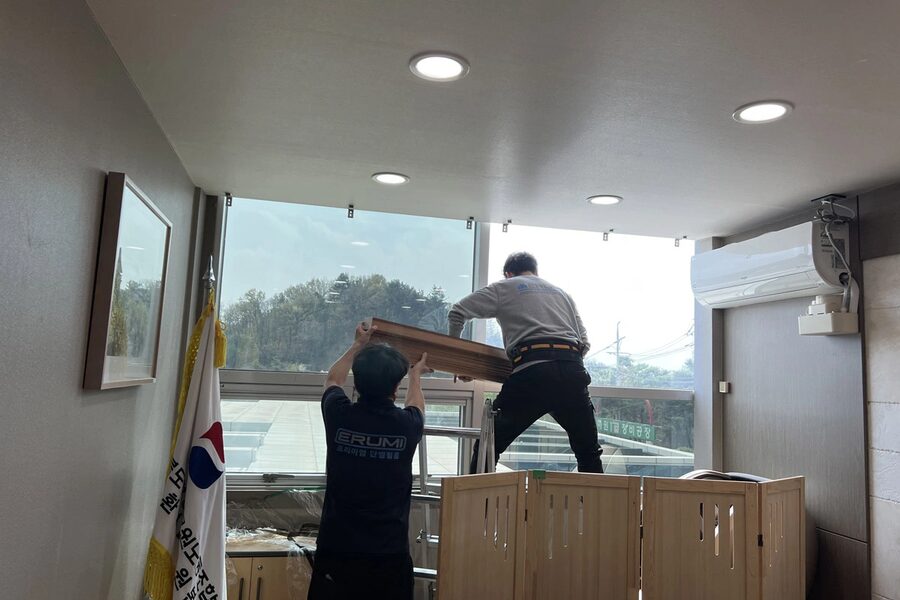 시공팀 두 명이 사다리 위에서 통유리에 필름을 붙이는 모습