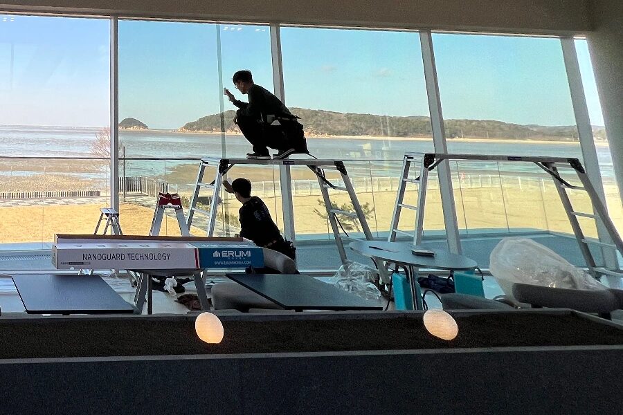 시공팀 두 명이 사다리 위에서 넓은 통유리에 필름을 붙이는 모습